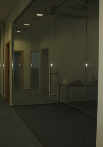 Przesuwne drzwi szklane w biurze, widoczne odbicie w szkle, minimalistyczny design, metalowy uchwyt, korytarz w tle.