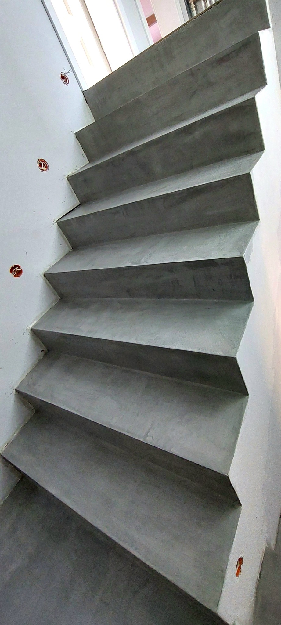 Betonowe schody o minimalistycznym wyglądzie z widocznymi puszkami elektrycznymi w ścianie, świeżo po wykonaniu.