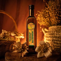 TOVPIKART Robert Towpik - Butelka oleju rzepakowego 0.5l na drewnianej desce, otoczona kwiatami i koszykami w ciepłym oświetleniu. Produkt spożywczy w aranżacji.