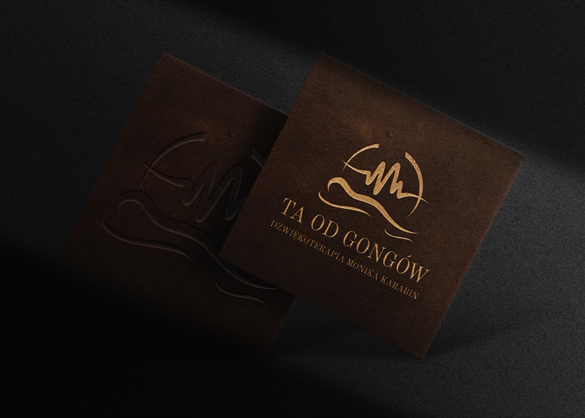Dwie brązowe wizytówki z wytłoczonym i złotym logo oraz napisem 'TA OD GONGÓW DŹWIĘKOTERAPIA MONIKA KARABIN' na czarnym teksturowanym tle.