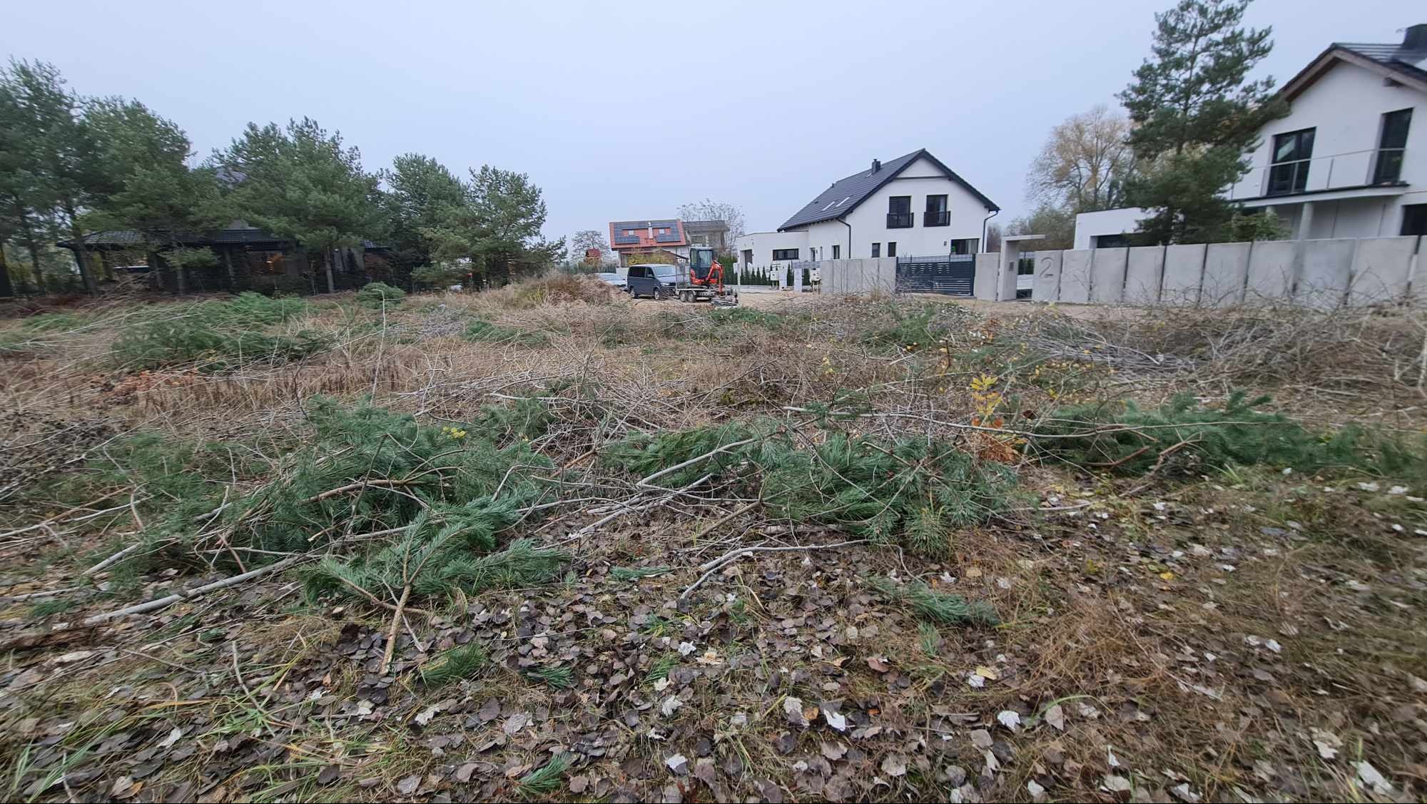 Teren w Dusznikach po wycince drzew i krzewów, przygotowany pod nowe nasadzenia, z widocznym minikoparką w tle.