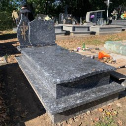 Usługi Kamieniarskie Bartosz Wandas - Granitowy pomnik z wygrawerowanym krzyżem i napisem 'Jezu ufam Tobie', otoczony jesiennymi liśćmi na cmentarzu, widoczne narzędzia i materiały budowlane.