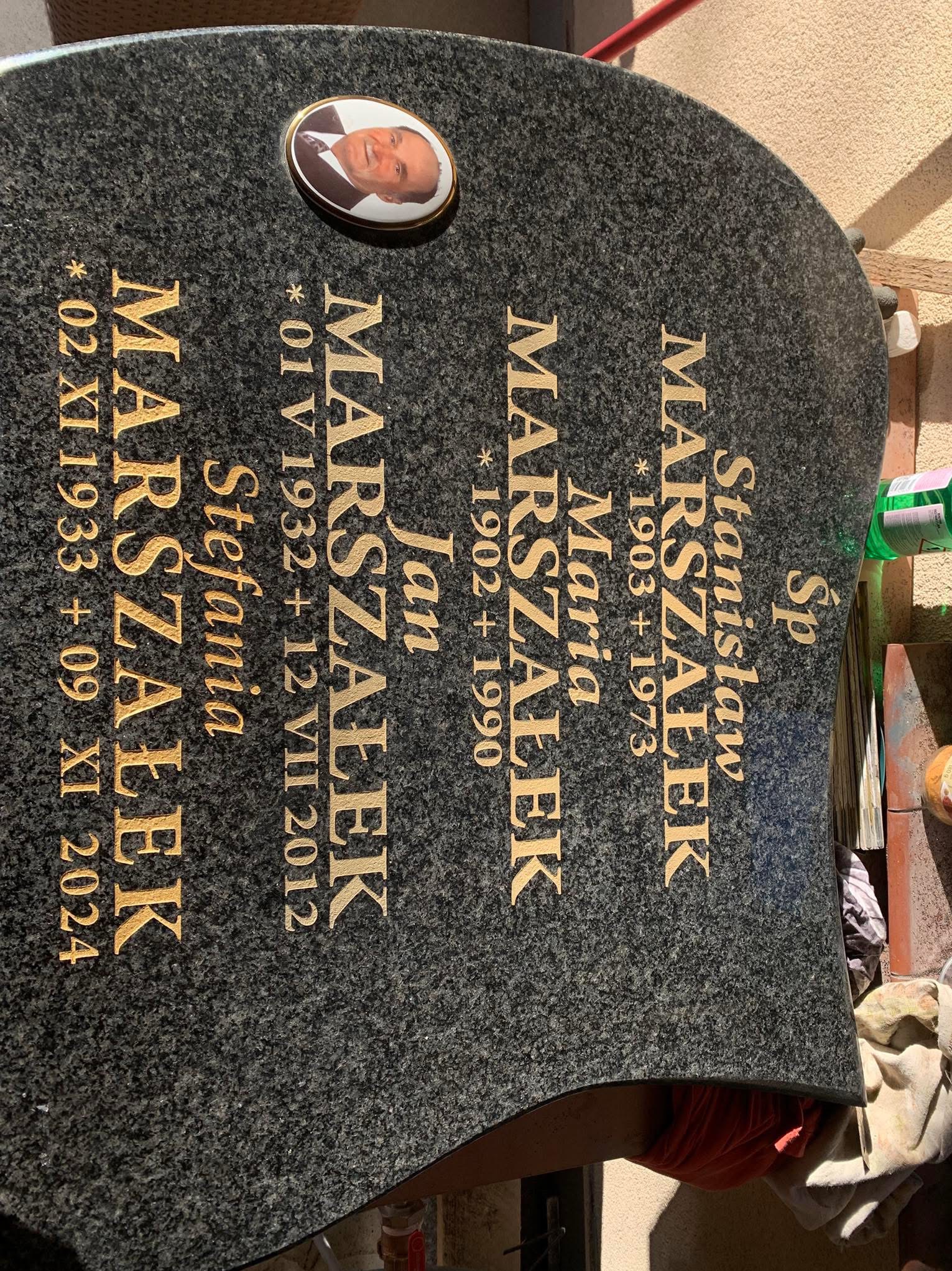 Granitowy pomnik nagrobny z wygrawerowanymi złotymi literami nazwiska Marszałek i datami urodzin oraz śmierci członków rodziny, z portretem jednego z nich, wykonany w Barcicach Dolnych.