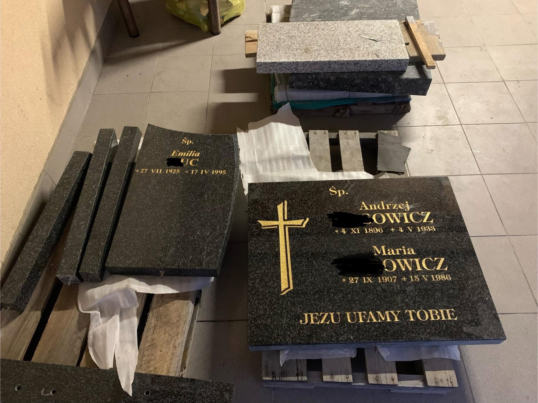 Przygotowane do montażu elementy pomnika z ciemnego granitu, z wygrawerowanymi złotymi literami i krzyżem, leżące na drewnianych paletach w pomieszczeniu.