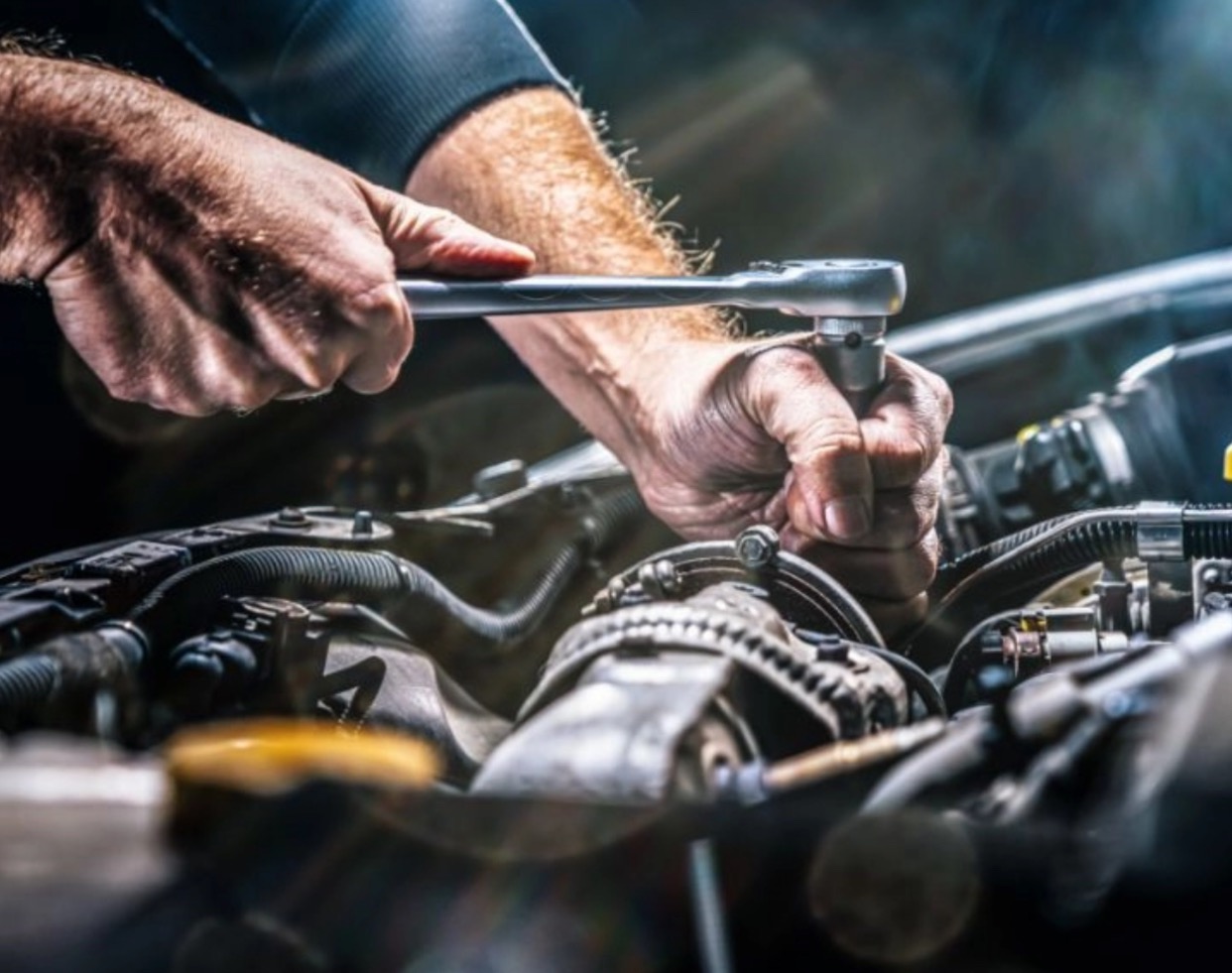 Mechanik dokręca śrubę w silniku samochodowym za pomocą klucza nasadowego, widoczne przewody i elementy silnika w zbliżeniu.