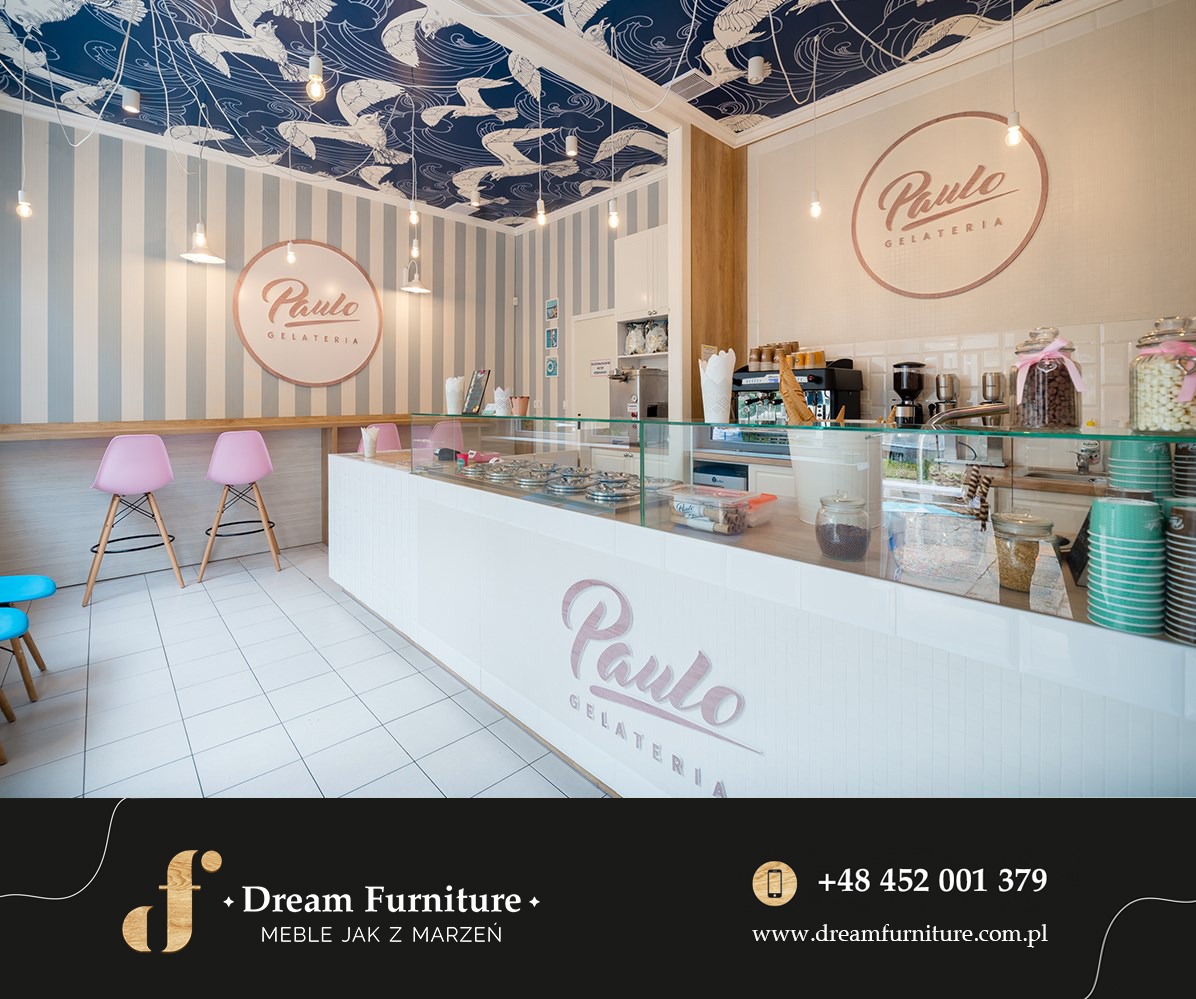 Wnętrze lodziarni Paulo Gelateria z białym, frezowanym blatem na wymiar, różowe krzesła barowe, sufit z motywem ptaków i logo firmy na ścianach.
