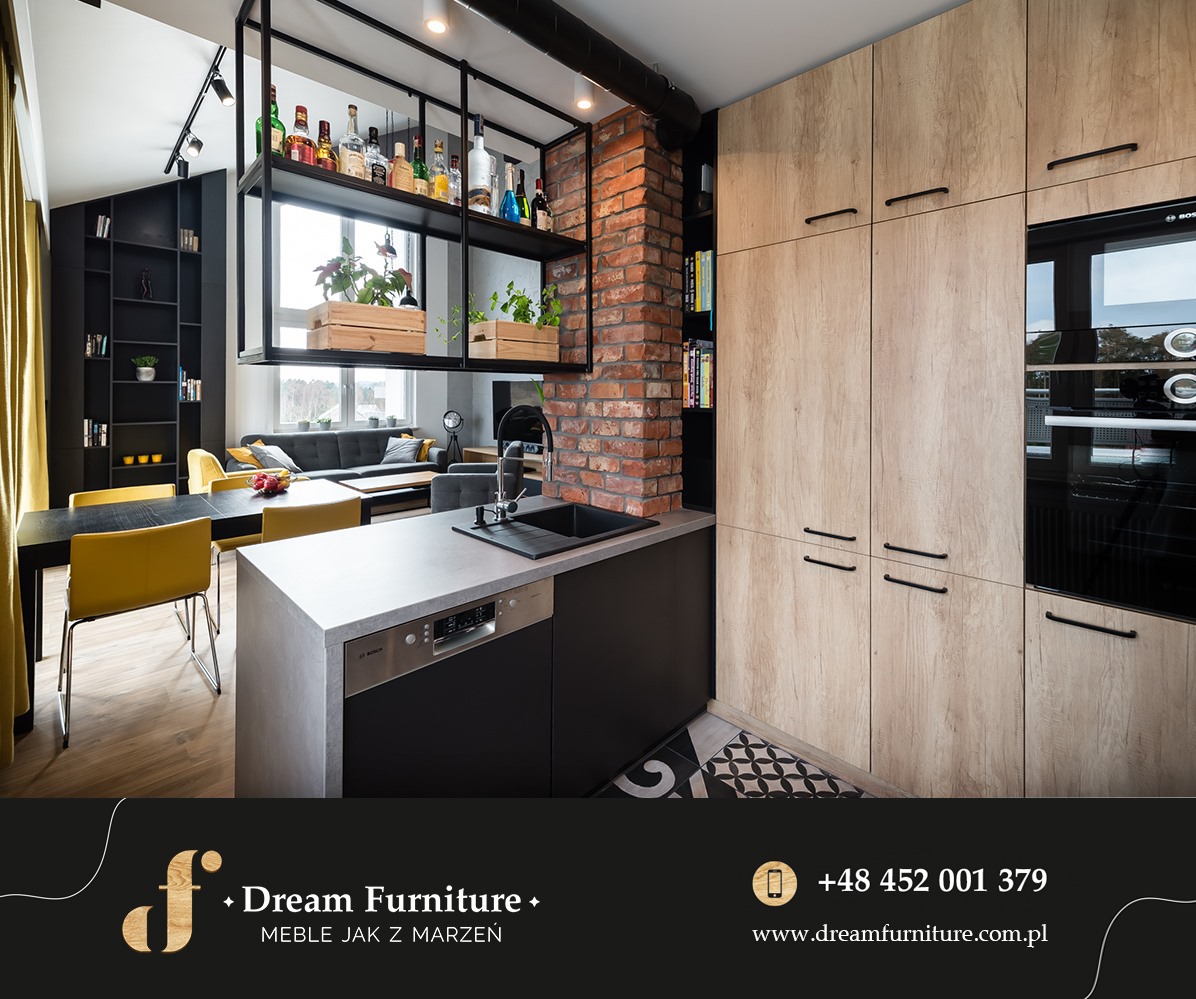 Nowoczesna kuchnia z drewnianymi frontami szafek, ceglanym filarem i czarnymi elementami, w tle salon z żółtymi akcentami.