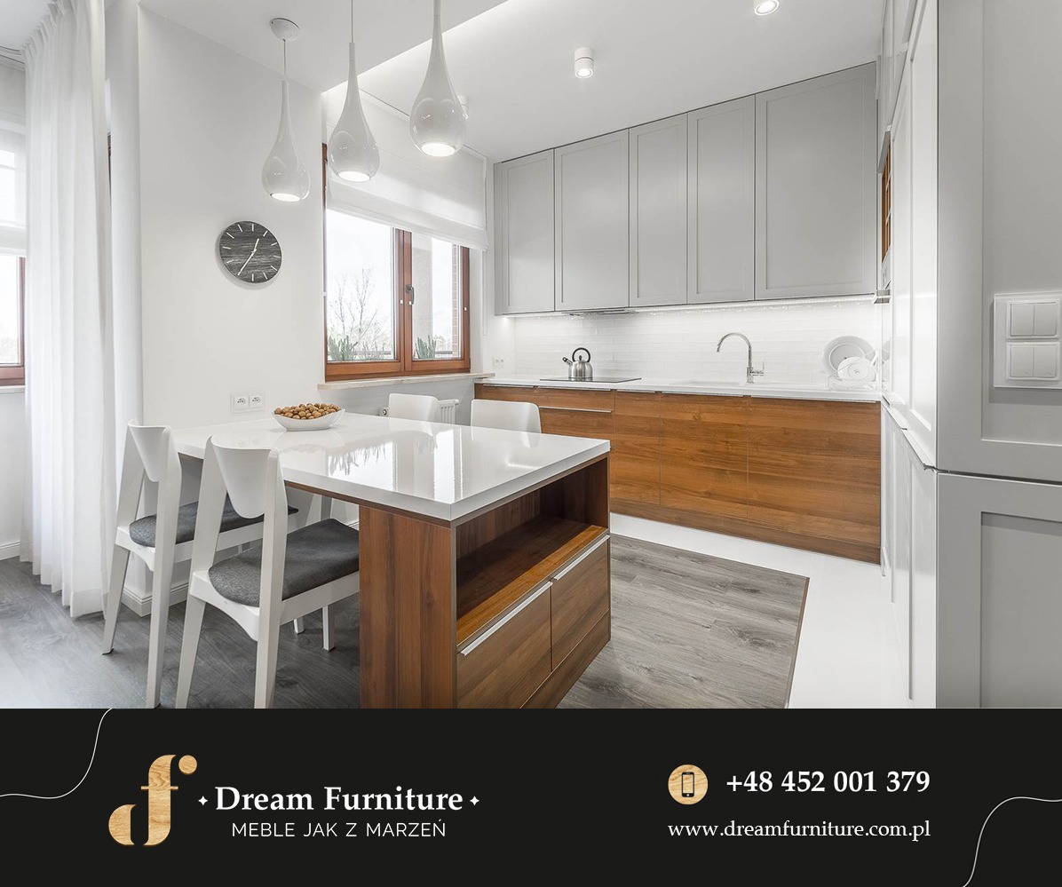 Jasna kuchnia z drewnianymi elementami: białe szafki górne, drewniane szafki dolne, biały blat, stół z wyspą i krzesła w stylu skandynawskim, widoczne oświetlenie punktowe i wiszące lampy.