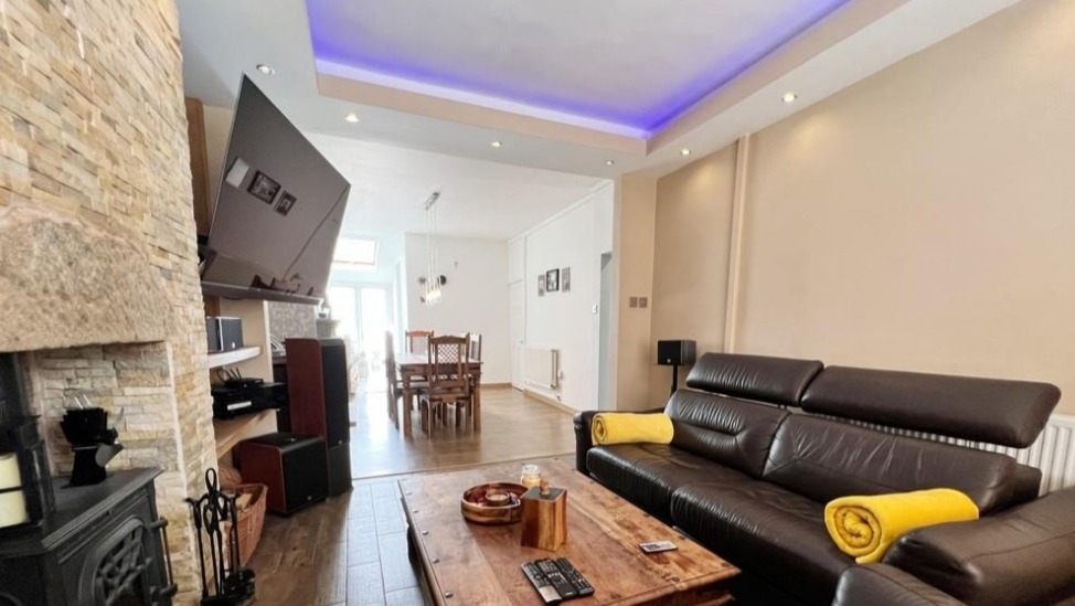 Salon z kamienną ścianą kominkową, brązową skórzaną sofą i widokiem na jadalnię, oświetlenie LED w suficie.