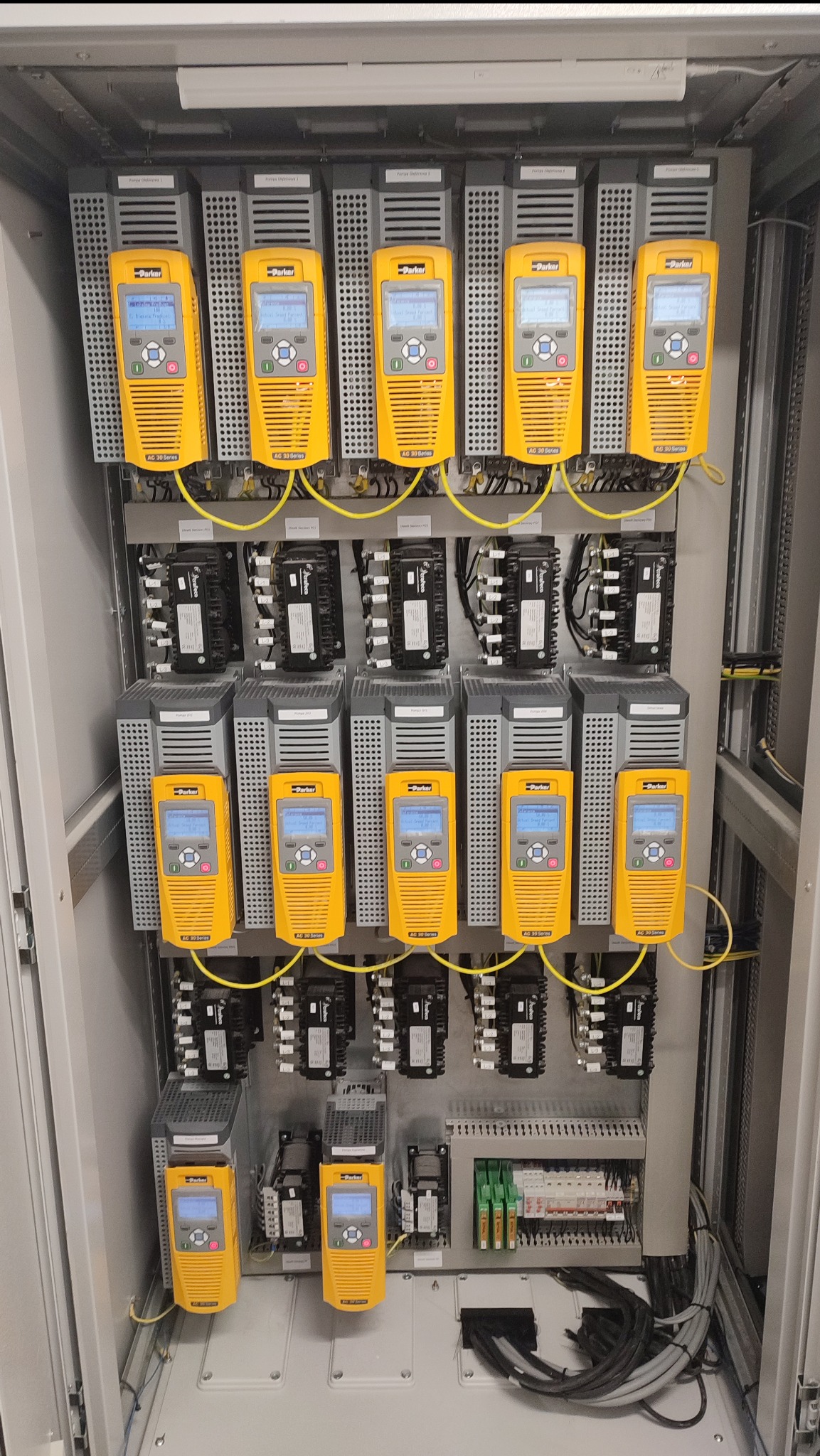 Rozdzielnica elektryczna z rzędami żółtych falowników Parker AC30 Series, podłączonych przewodami, widoczne również czarne styczniki i listwa zaciskowa z bezpiecznikami.