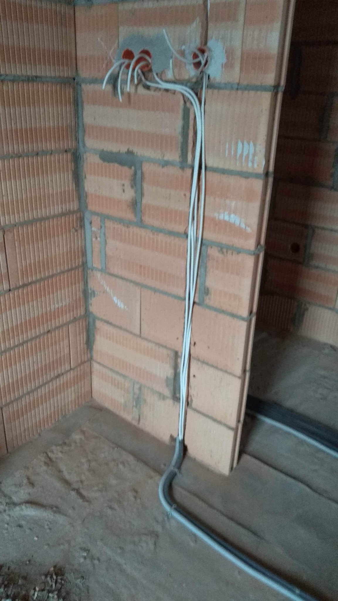 Surowe wnętrze w trakcie budowy: widoczne przewody elektryczne wychodzące ze ściany z pustaków, zabezpieczone peszlem przy podłodze, przygotowane do dalszych prac.