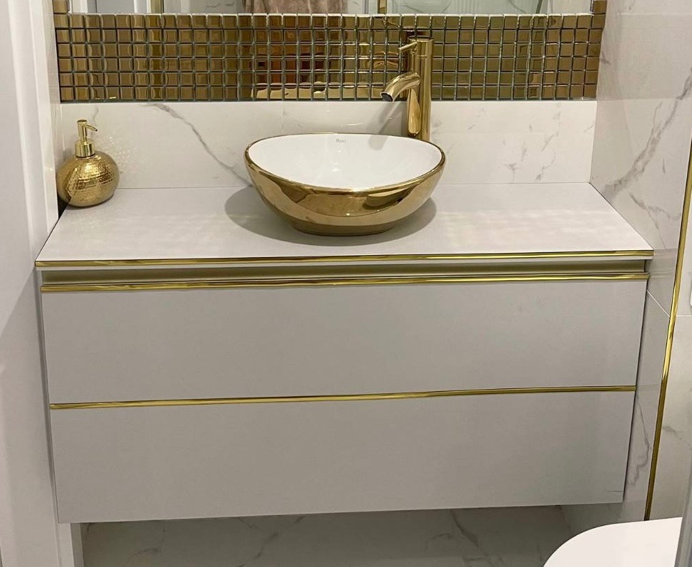 Elegancka łazienka z umywalką nablatową w kolorze złota, armaturą w tym samym odcieniu i szafką pod umywalką z subtelnymi złotymi akcentami, wykończona marmurowymi płytkami.