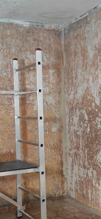 Przygotowanie ściany do prac wykończeniowych: widoczna drabina aluminiowa i fragment ściany z widocznymi śladami po usunięciu starej farby lub tapety, ukazujący nierówności i przygotowanie...