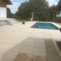 BUILDERS GROUP SPÓŁKA Z OGRANICZONĄ ODPOWIEDZIALNOŚCIĄ - Wyłożony jasnymi płytami taras z basenem w tle, widoczne schody z kamienia i narzędzia budowlane, dom z drewnianymi elementami.