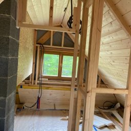 BUILDERS GROUP SPÓŁKA Z OGRANICZONĄ ODPOWIEDZIALNOŚCIĄ - Konstrukcja drewniana poddasza w trakcie ocieplania, widoczne elementy więźby, okno dachowe i izolacja w rolce, zabezpieczona folią podłoga.