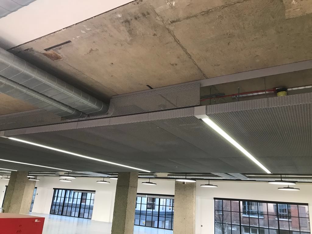 Sufit podwieszany rastrowy z oświetleniem LED w nowoczesnym biurze, widoczne instalacje wentylacyjne pod surowym betonowym stropem.