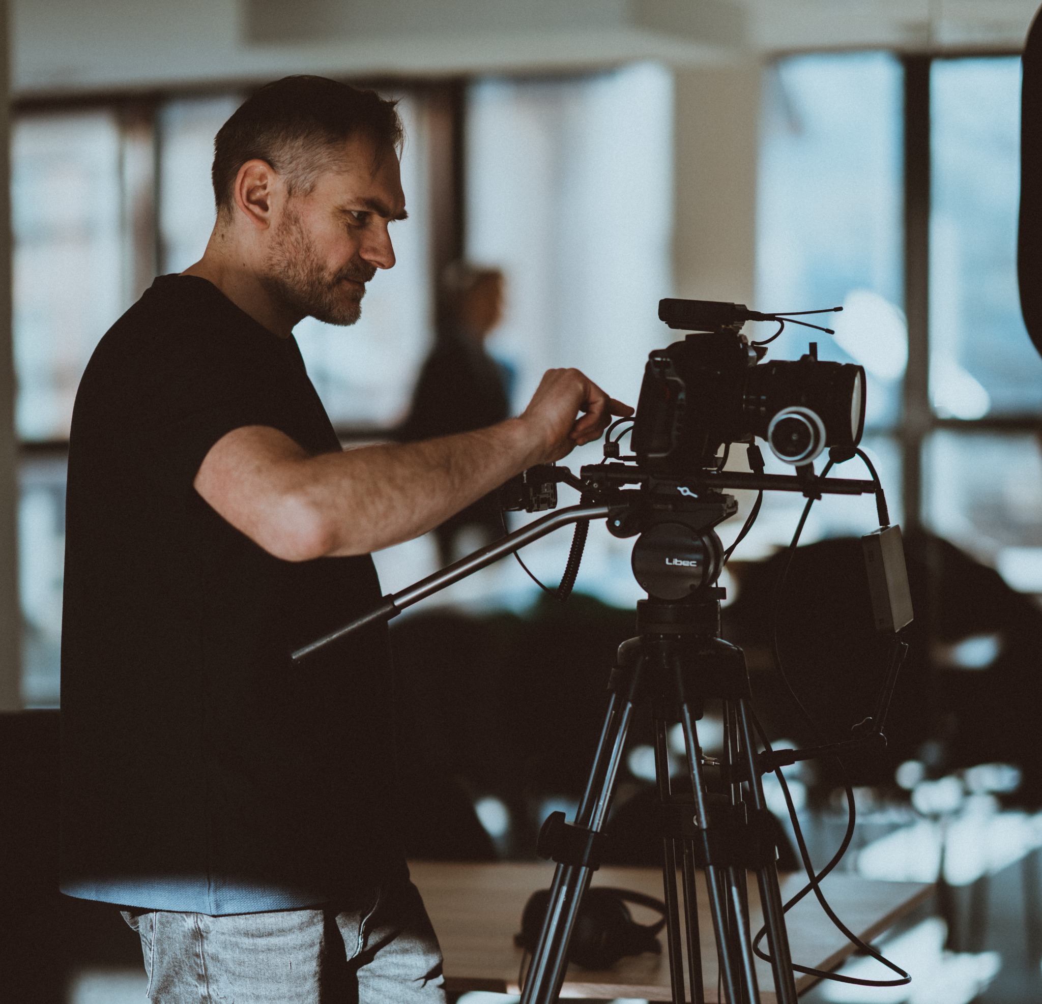 Operator filmowy reguluje ustawienia kamery Libec na statywie, przygotowując się do nagrania sceny w jasnym pomieszczeniu.
