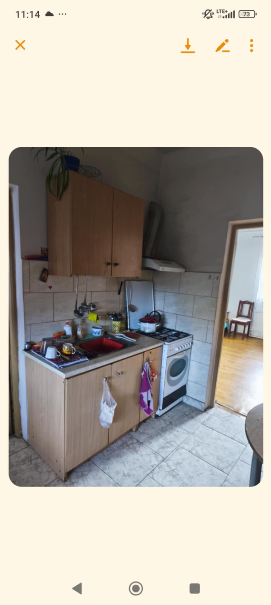 Wnętrze kuchni przed remontem: widok na zabudowę kuchenną z czerwonym zlewem, kuchenkę gazową i płytki na ścianach. Widoczny bałagan i zużycie.