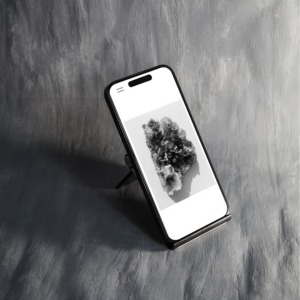 Smartfon z wyświetloną grafiką przypominającą chmurę lub abstrakcyjny wzór na białym tle, umieszczony na czarnym stojaku, z szarym, teksturowanym tłem.