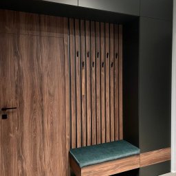 FORMHAUS Michał Ozga - Nowoczesna zabudowa przedpokoju z drewnianymi lamelami, wieszakami i zielonym siedziskiem, całość w stonowanej kolorystyce.