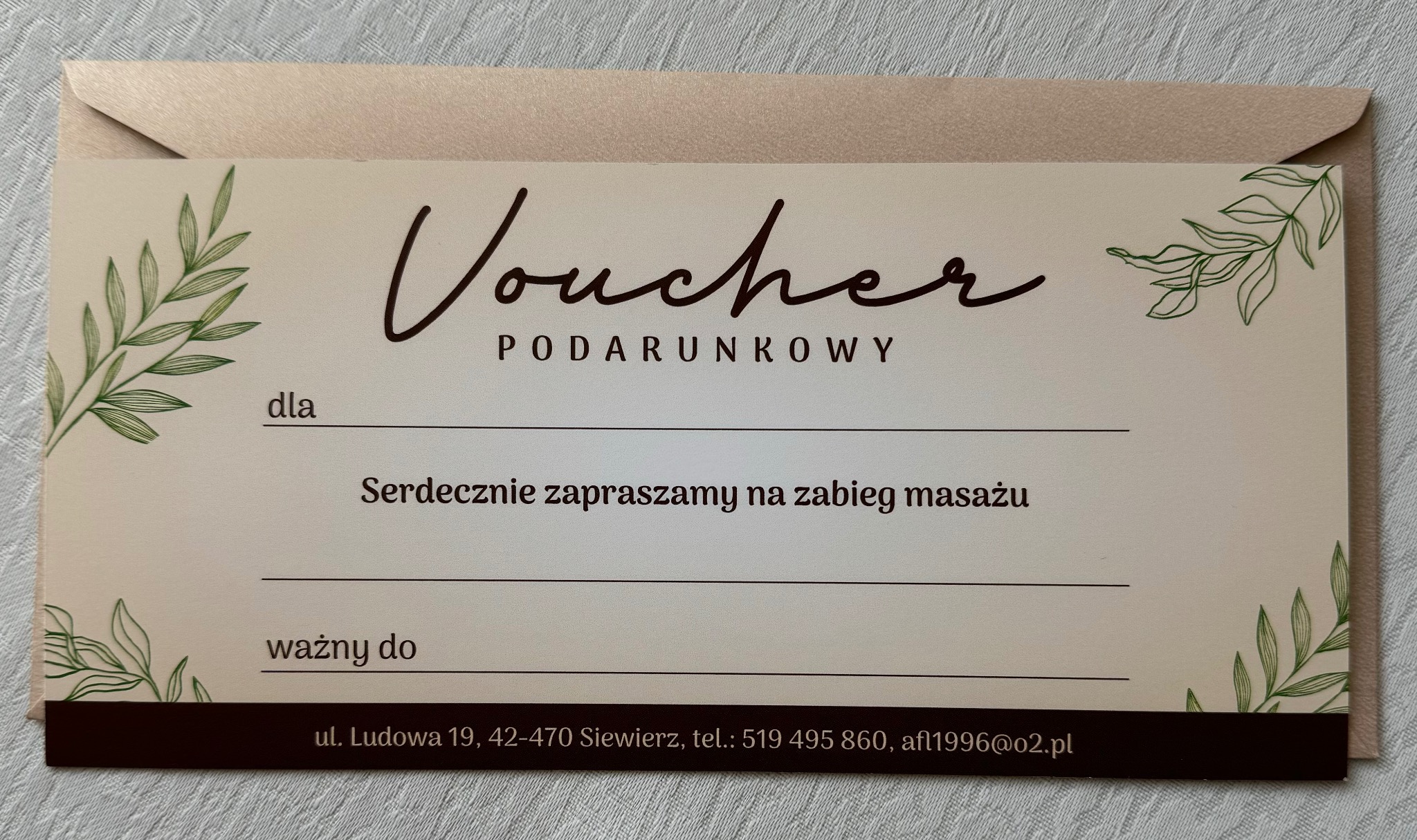 Kremowy voucher prezentowy na zabieg masażu z zielonymi motywami roślinnymi i kopertą w tle.