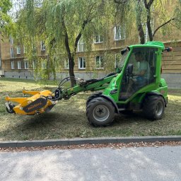 RoboExpert - Operator w zielonym traktorze Avant 745 z żółtą kosiarką bijakową Müthing na trawniku przed budynkiem mieszkalnym.