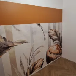 Wnętrze pokoju z panelami podłogowymi ułożonymi w jodełkę, ścianą z białym i brązowym pasem oraz tapetą w tropikalne liście i ptaki.