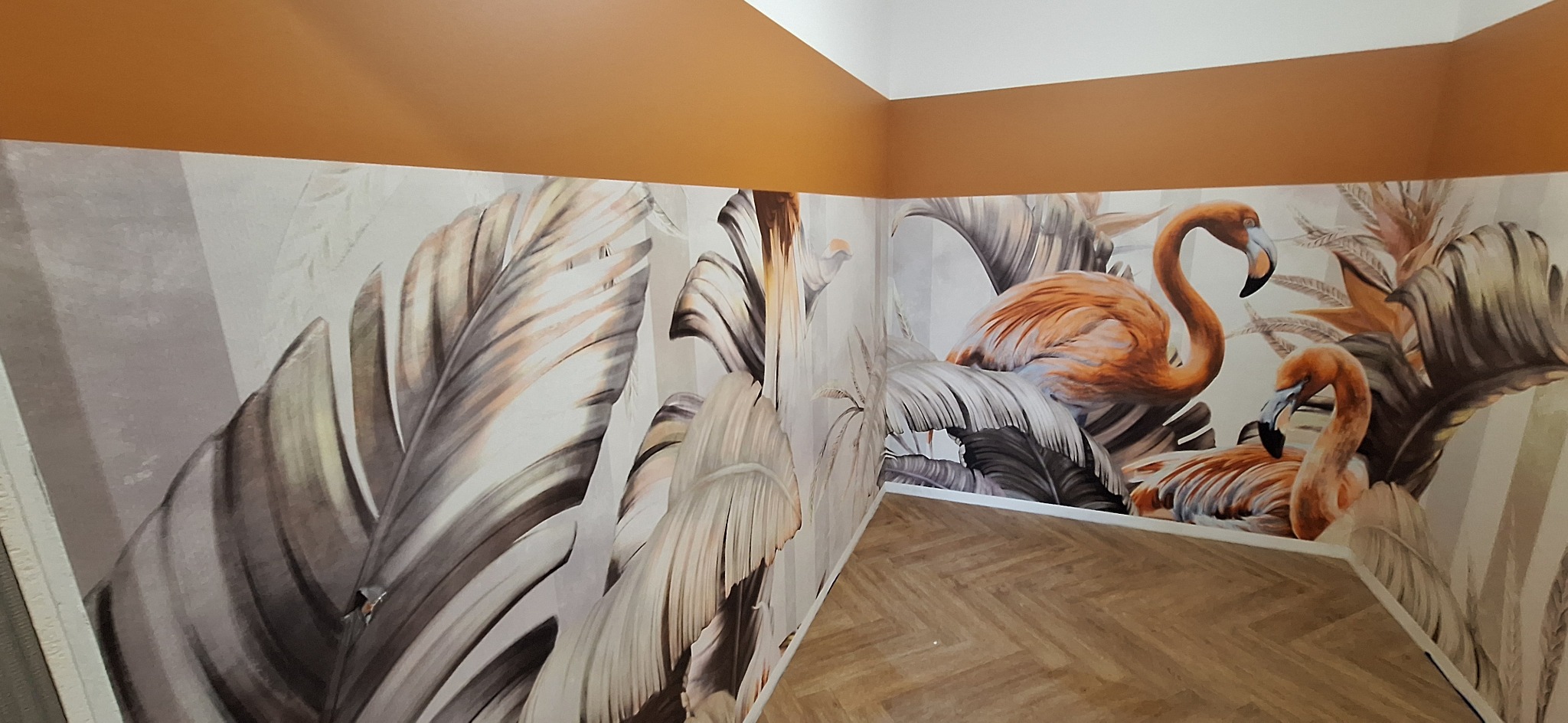 Pokój po odświeżeniu z fototapetą przedstawiającą flamingi i tropikalne liście, pomalowany górny pas ściany na kolor miodowy, podłoga wyłożona panelami w jodełkę.