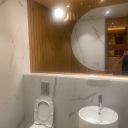 KATRUK Technologies - Nowoczesna łazienka we Wrocławiu z marmurowymi płytkami, okrągłym lustrem z oświetleniem LED, wiszącą toaletą z podtynkowym systemem spłukiwania i umywalką na postumencie.