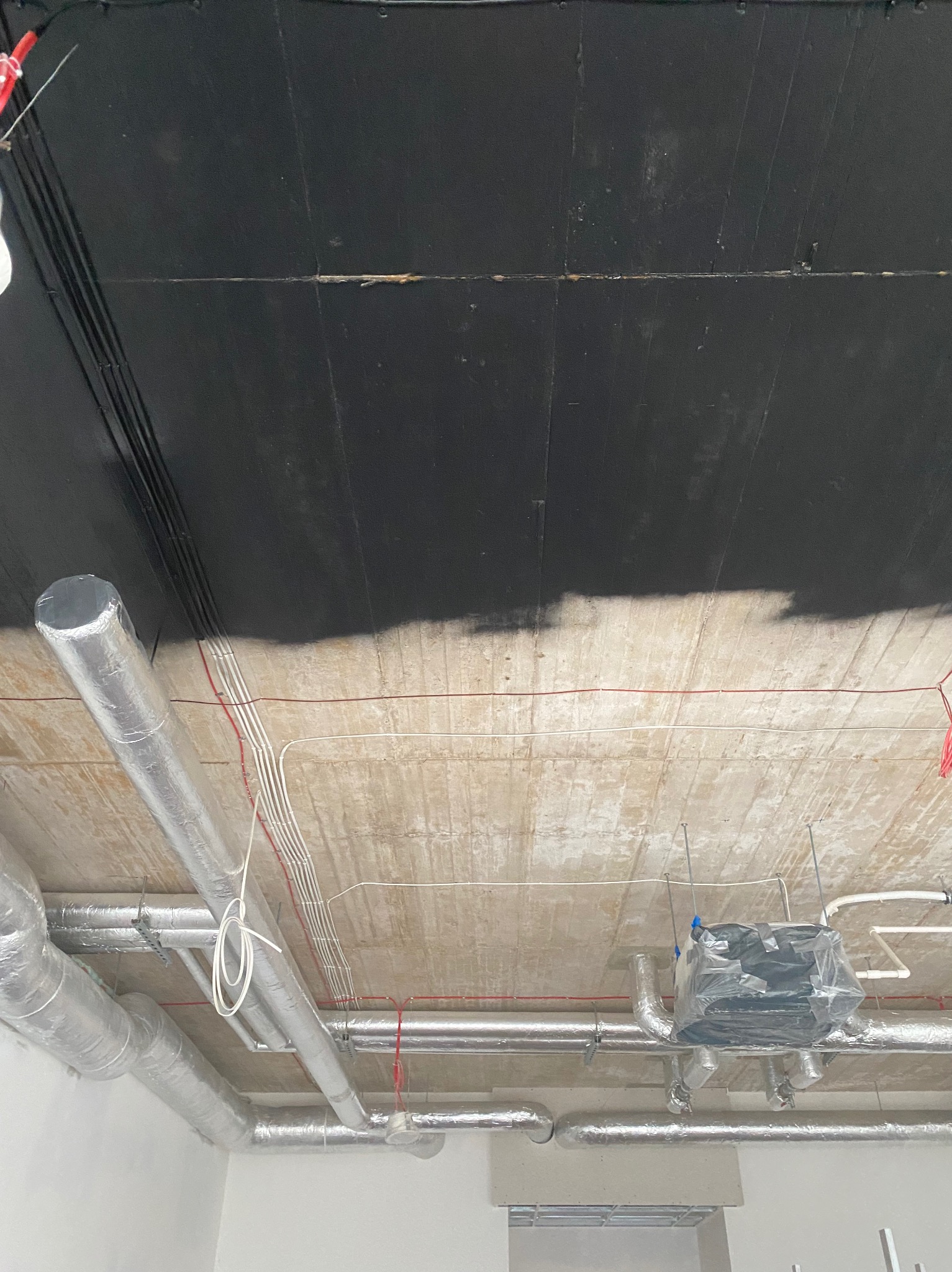 Częściowo pomalowany na czarno sufit z widocznymi rurami wentylacyjnymi w srebrnej izolacji, okablowaniem elektrycznym i elementami instalacji klimatyzacyjnej.