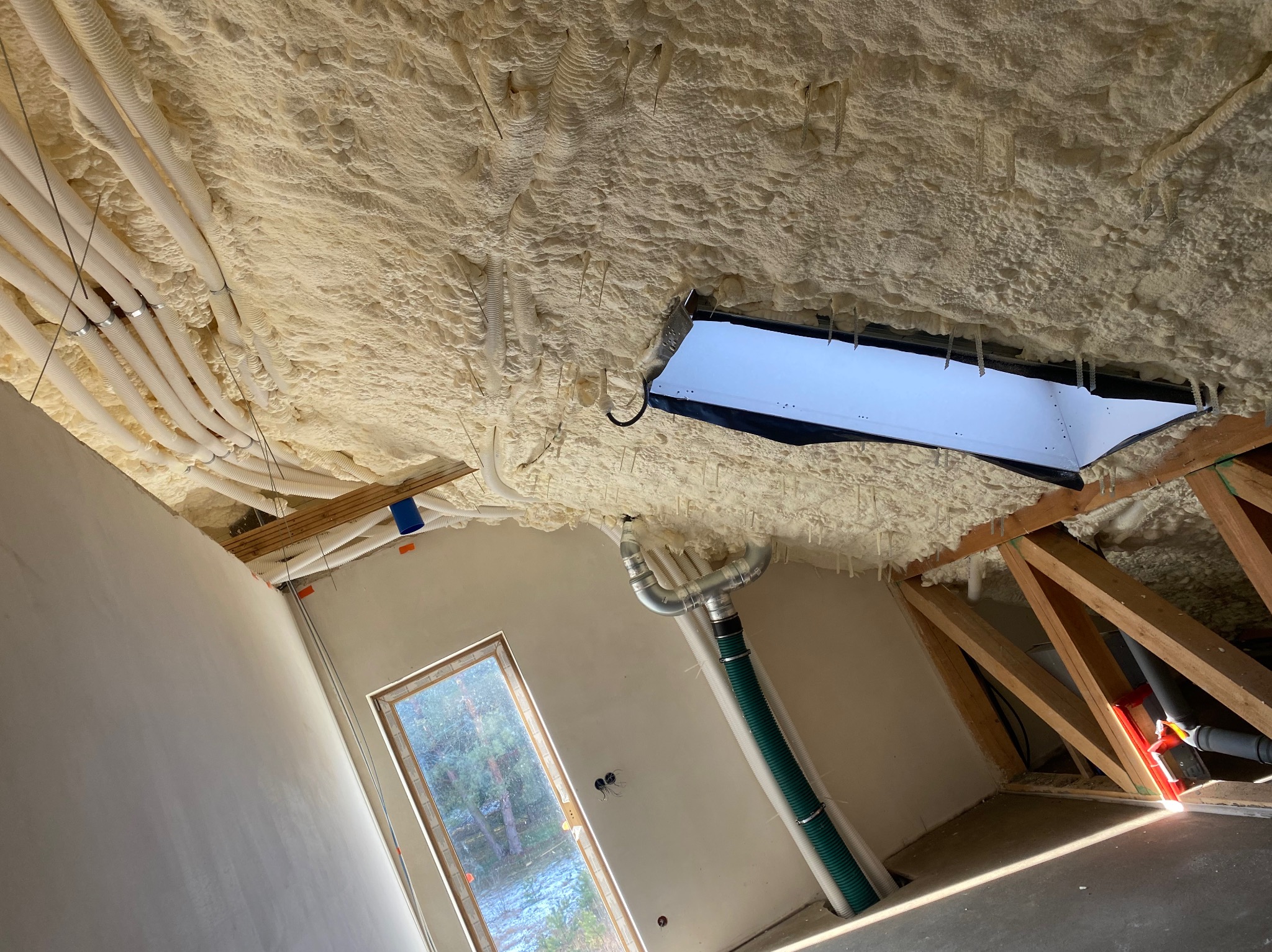 Poddasze z ociepleniem pianą PUR, widoczne przewody wentylacyjne, okno dachowe i fragment ściany przed wykończeniem.