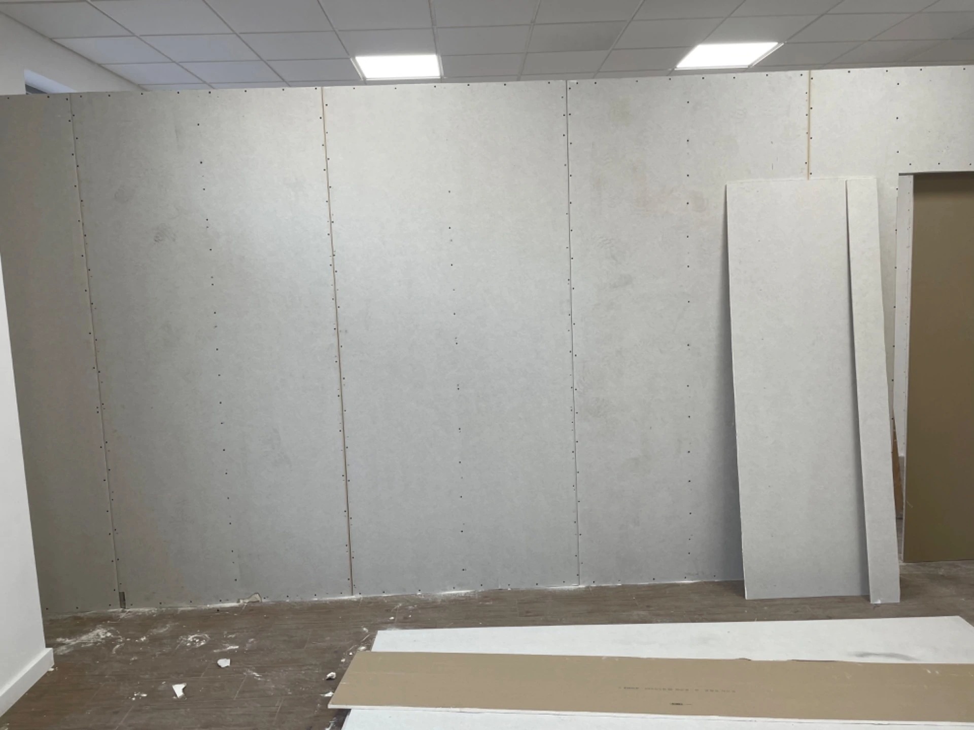 Wnętrze w trakcie montażu ścian z płyt kartonowo-gipsowych, widoczne płyty stojące przy ścianie, ślady po wkrętach na powierzchni płyt.