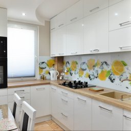 Zakład Stolarski STOLUX - Nowoczesna, jasna kuchnia z białymi, lakierowanymi frontami, drewnianym blatem i szklanym panelem ściennym z motywem cytryn i lodu, widok na płytę grzewczą i zlew.
