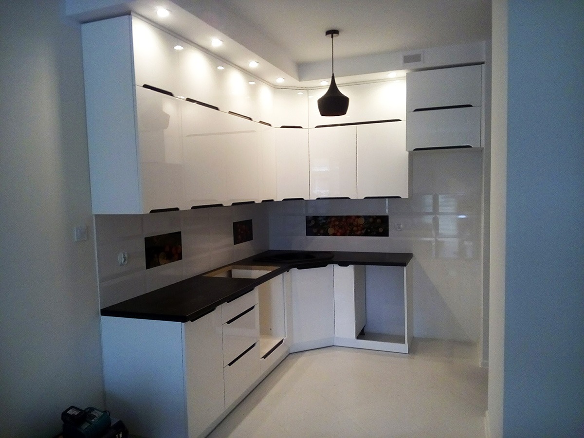 Biała, nowoczesna kuchnia na wymiar z czarnym blatem, oświetleniem punktowym i wiszącą lampą w kształcie stożka, widok z niskiego kąta.