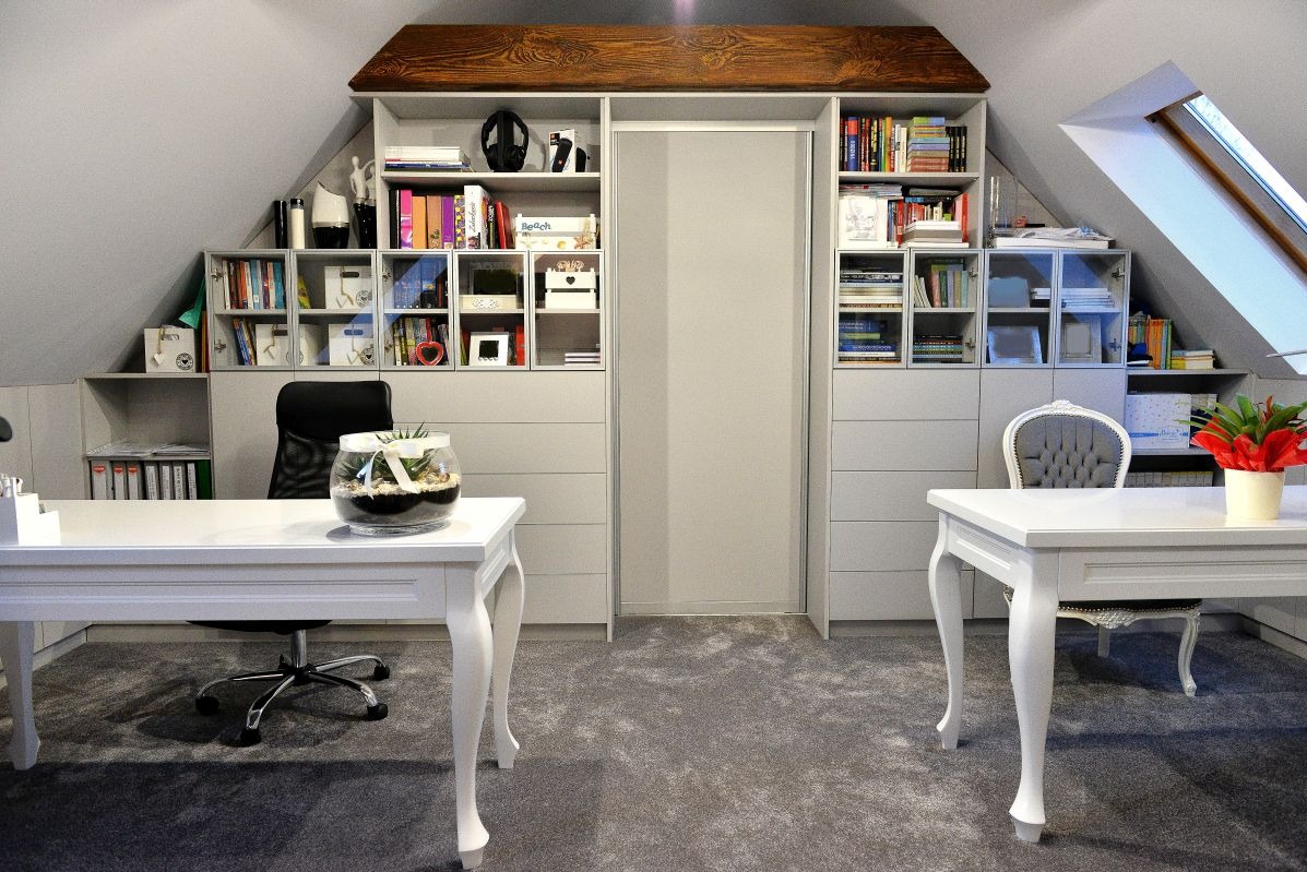 Biuro w Suwałkach na poddaszu ze ścianą regałów na wymiar i białymi biurkami na giętych nogach, oświetlone światłem dziennym z okna dachowego.