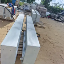 Dwa elementy konstrukcyjne pomalowane na szaro, leżące na paletach na piaszczystym podłożu, prawdopodobnie po piaskowaniu i malowaniu proszkowym.