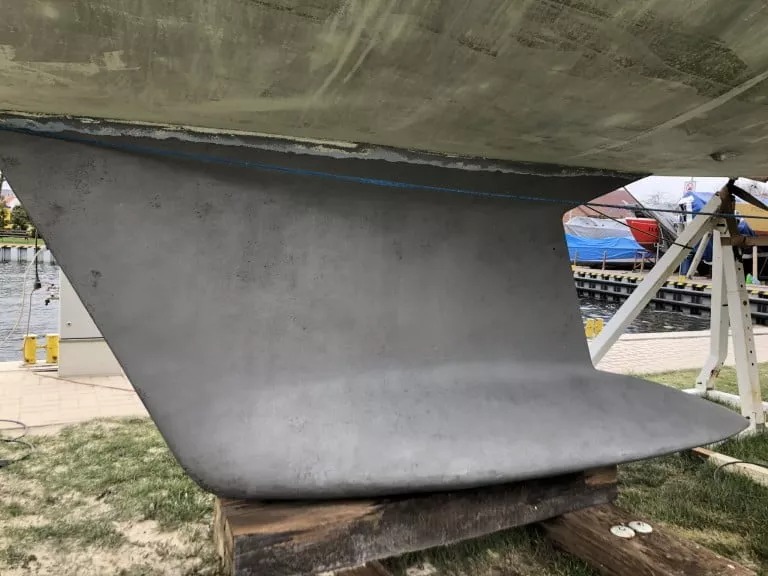 Szary kil jachtu po renowacji, zabezpieczony przed wodą, widoczna linia wodna i drewniane podpory