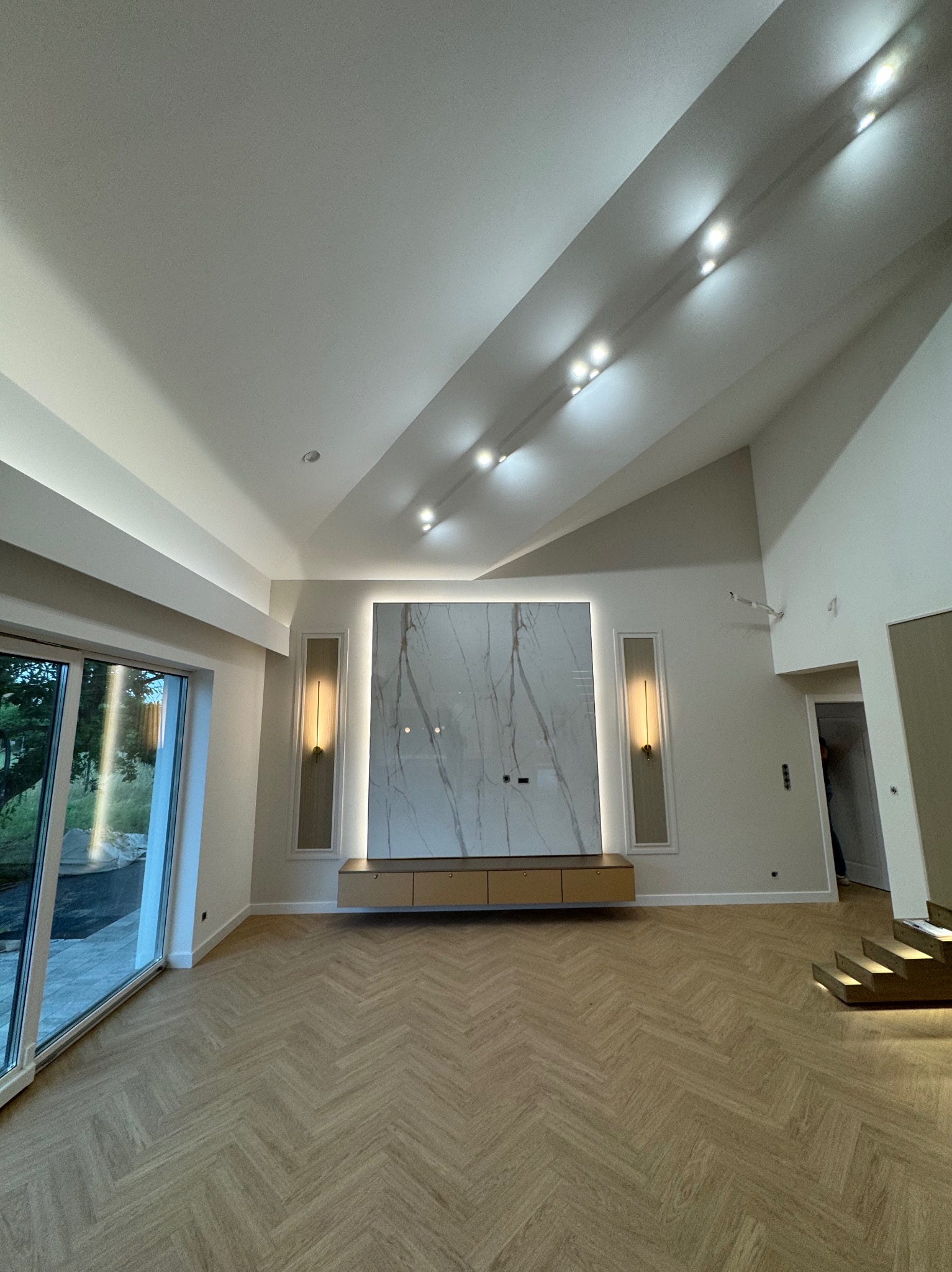 Jasne wnętrze z parkietem w jodełkę, marmurową ścianą TV i oświetleniem LED. Nowoczesny design z dużym oknem i schodami z podświetleniem.