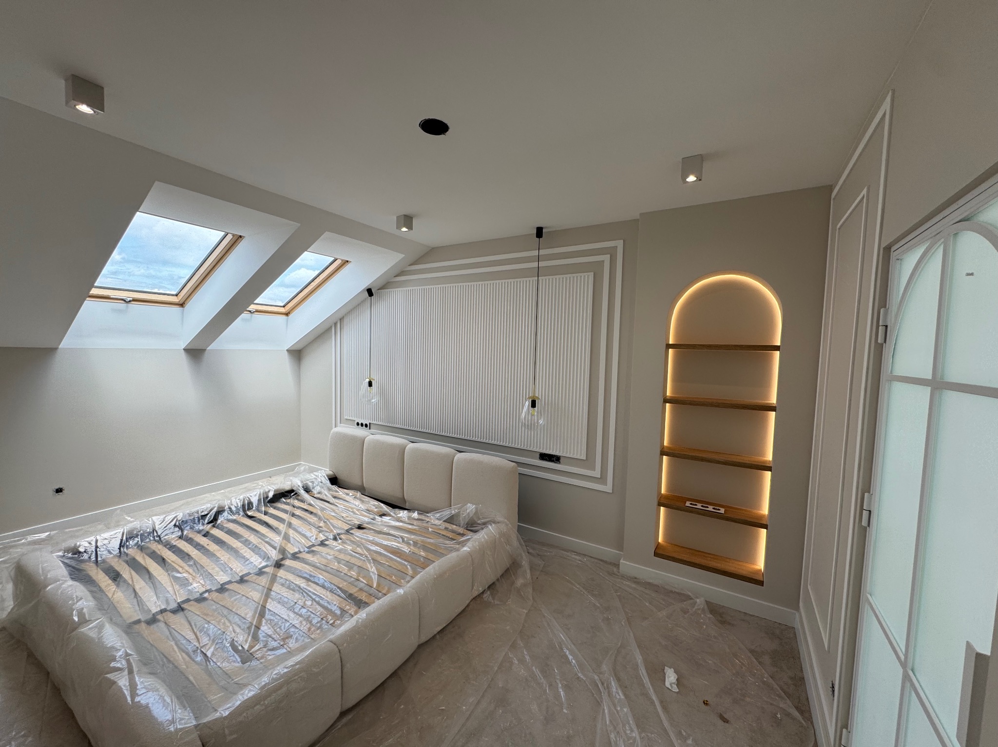 Wykończone poddasze ze skośnymi oknami dachowymi i dekoracyjną ścianą za łóżkiem. Wnęka z półkami podświetlona ledami. Podłoga zabezpieczona folią malarską.