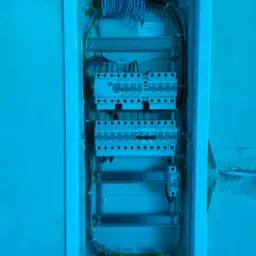 Wewnętrzny widok skrzynki rozdzielczej podtynkowej z zainstalowanymi bezpiecznikami EATON, przewodami i listwami zaciskowymi, widoczne kable wychodzące ze ściany.