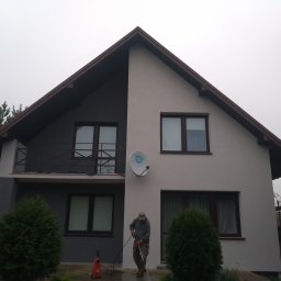 MarHor Renovations - Dwukondygnacyjny dom jednorodzinny z balkonem, czyszczony myjką ciśnieniową przez pracownika w odzieży roboczej, widoczna antena satelitarna na elewacji.