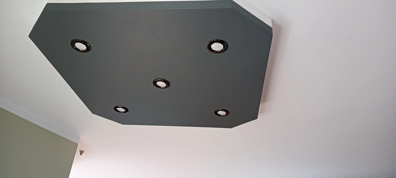 Szary, wielokątny podwieszany sufit z pięcioma okrągłymi lampami punktowymi, widok z dołu.