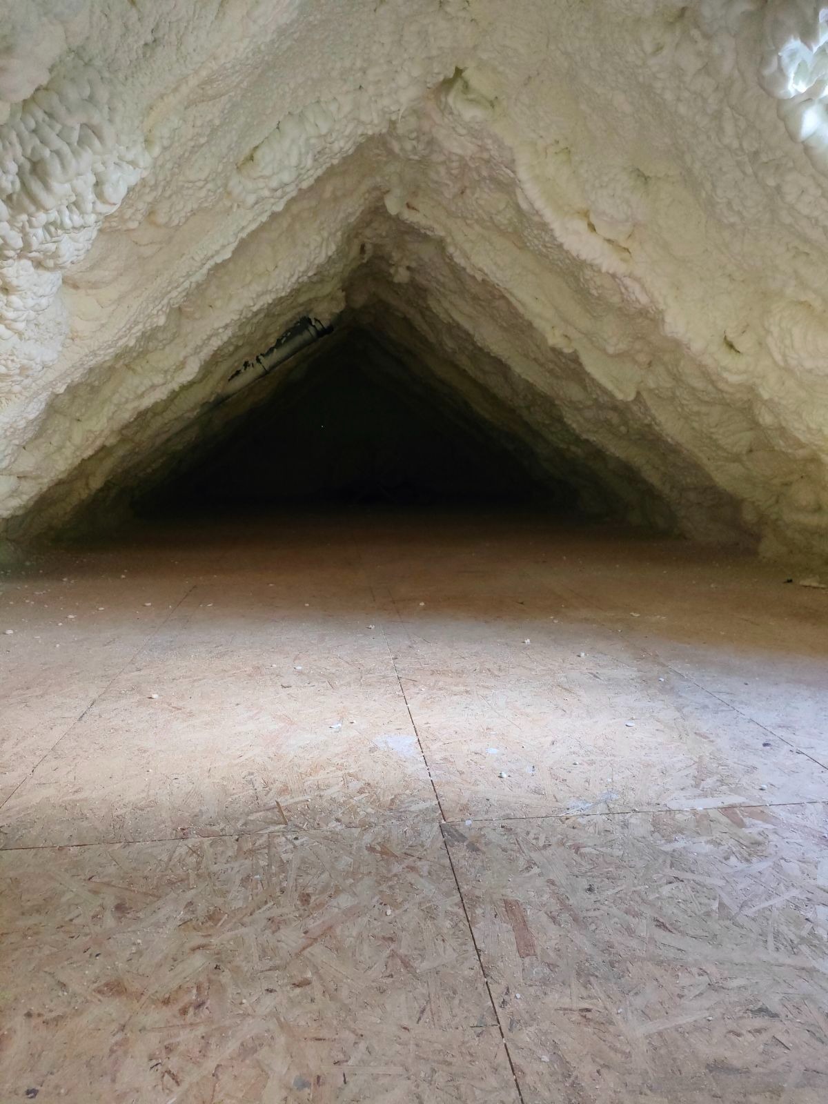 Poddasze ocieplone pianką, widok z poziomu podłogi, widoczna struktura pianki na skośnych ścianach i suficie, w tle ciemność.