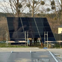 ZECO POZYTYWNA ENERGIA SPÓŁKA Z OGRANICZONĄ ODPOWIEDZIALNOŚCIĄ - Montaż paneli słonecznych na stelażu w ogrodzie, widoczne rusztowania i ekipa montażowa, w tle drzewa bez liści i fragment pokrywy basenowej z kałużami.