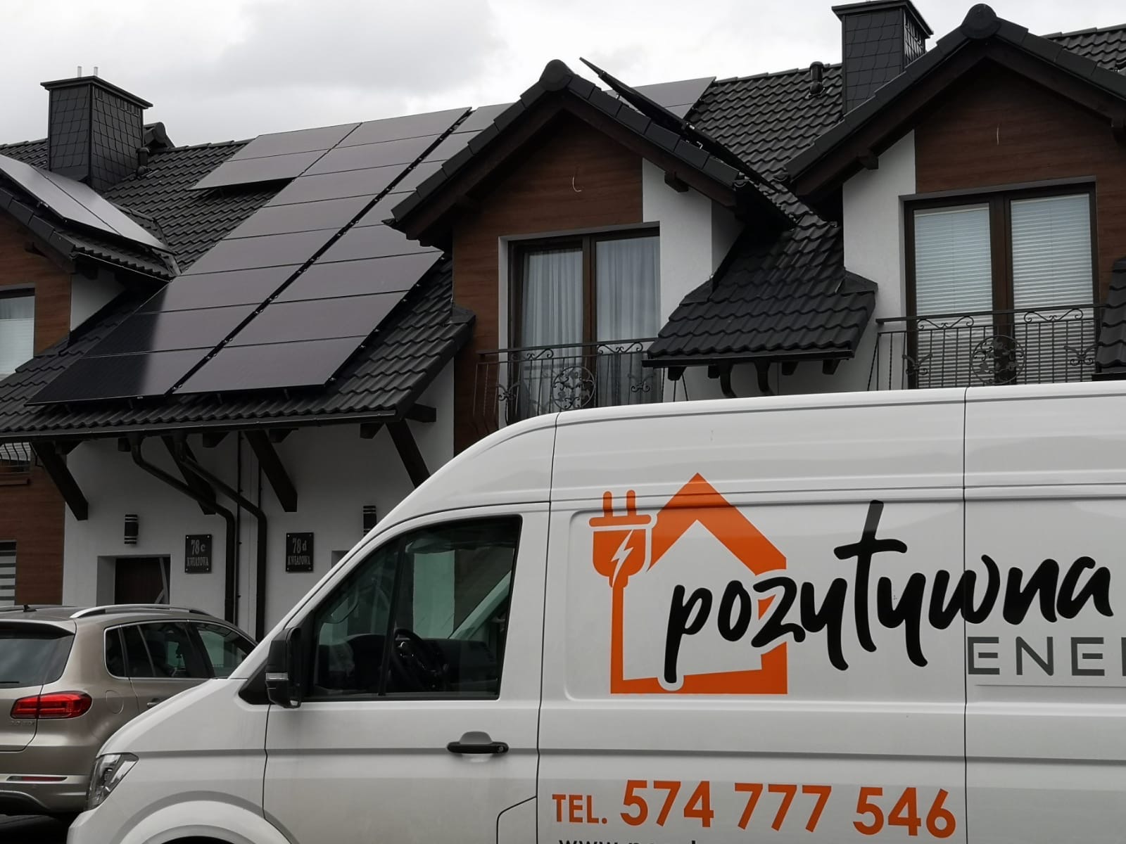Dom z panelami słonecznymi na dachu, widok z poziomu ulicy, z boku widoczny samochód dostawczy z logo firmy instalującej panele.
