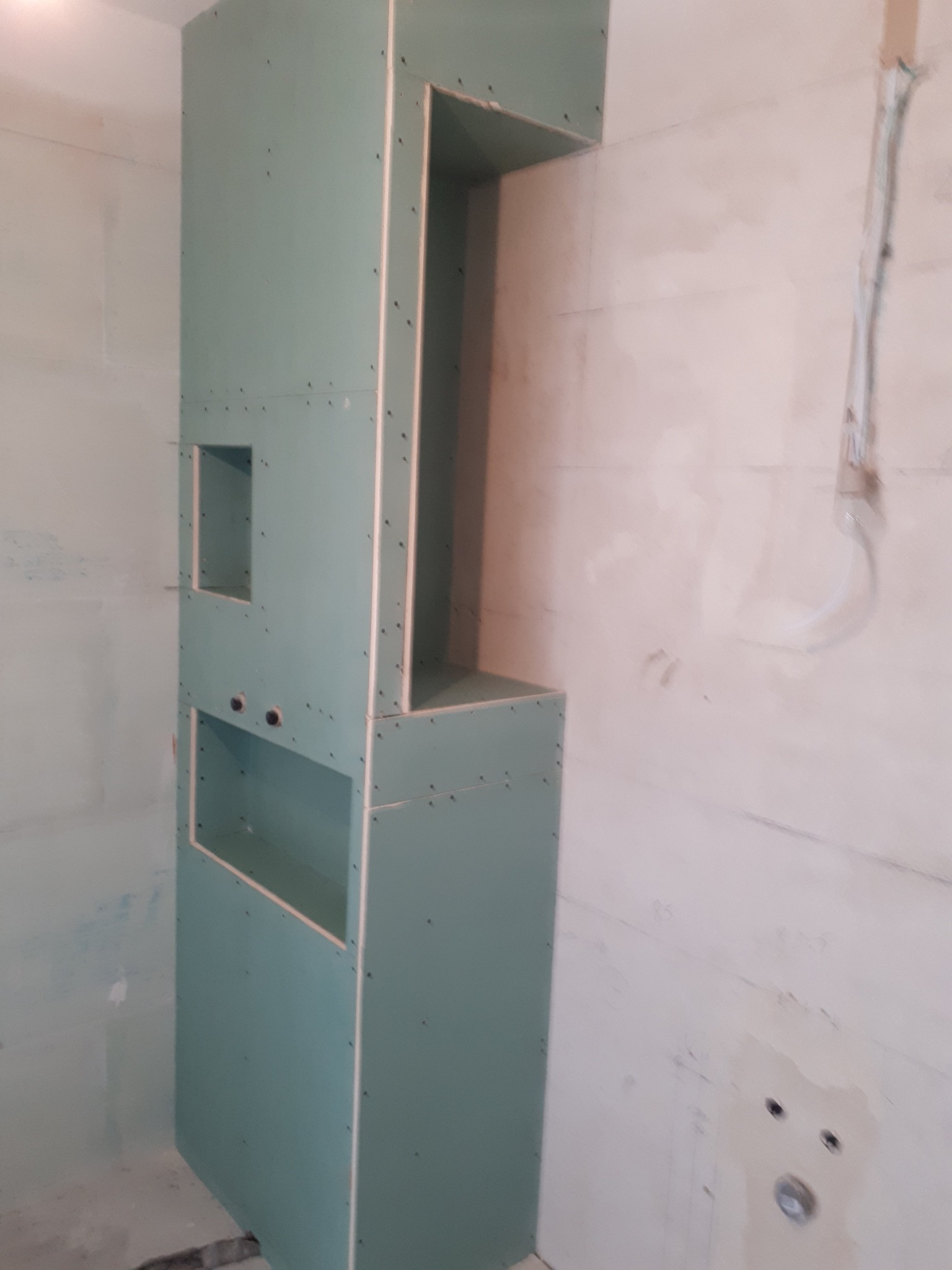 Konstrukcja z płyt gipsowo-kartonowych z otworami na instalacje, widoczna na tle surowej ściany w trakcie remontu.