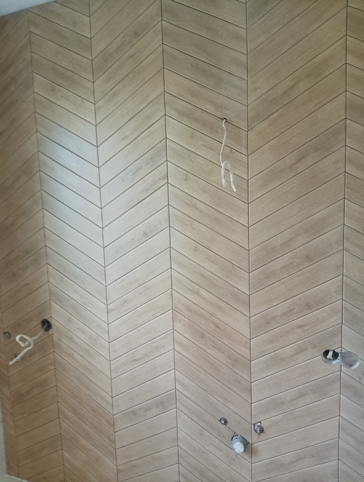 Ściana wyłożona drewnopodobnymi płytkami w jodełkę, z widocznymi otworami na instalacje elektryczne i hydrauliczne, w trakcie montażu.