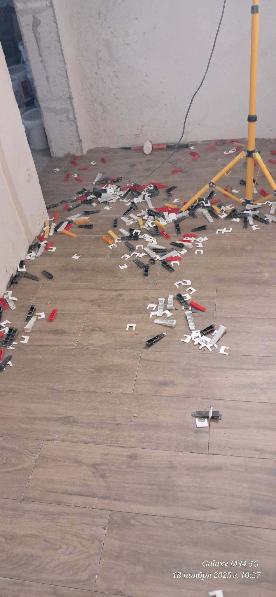 Ułożone płytki podłogowe z systemem poziomowania płytek (klipsy i kliny) w trakcie prac. Widoczna lampa budowlana.