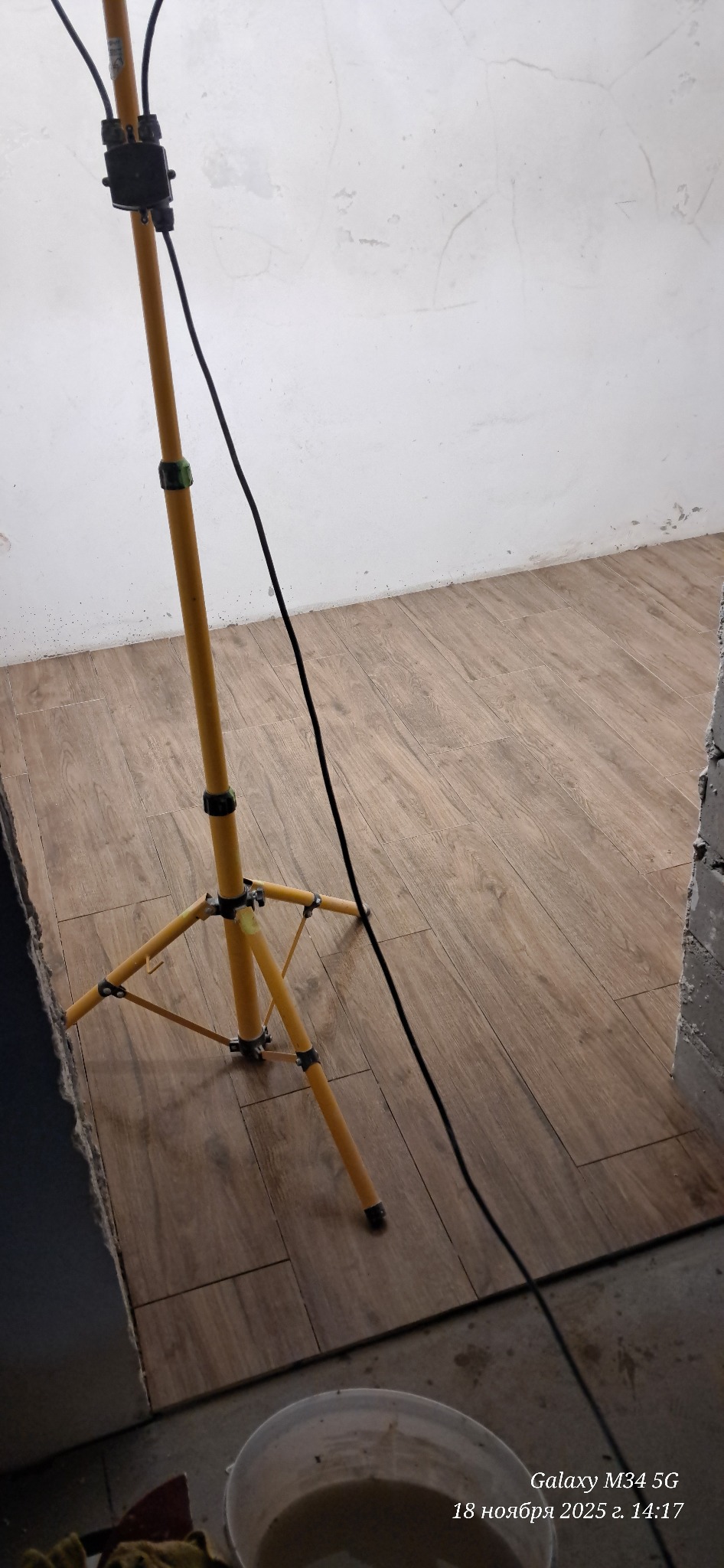 Ułożone panele podłogowe w odcieniach brązu, oświetlone lampą budowlaną. Widoczny fragment ściany w trakcie prac wykończeniowych i wiadro z zaprawą.