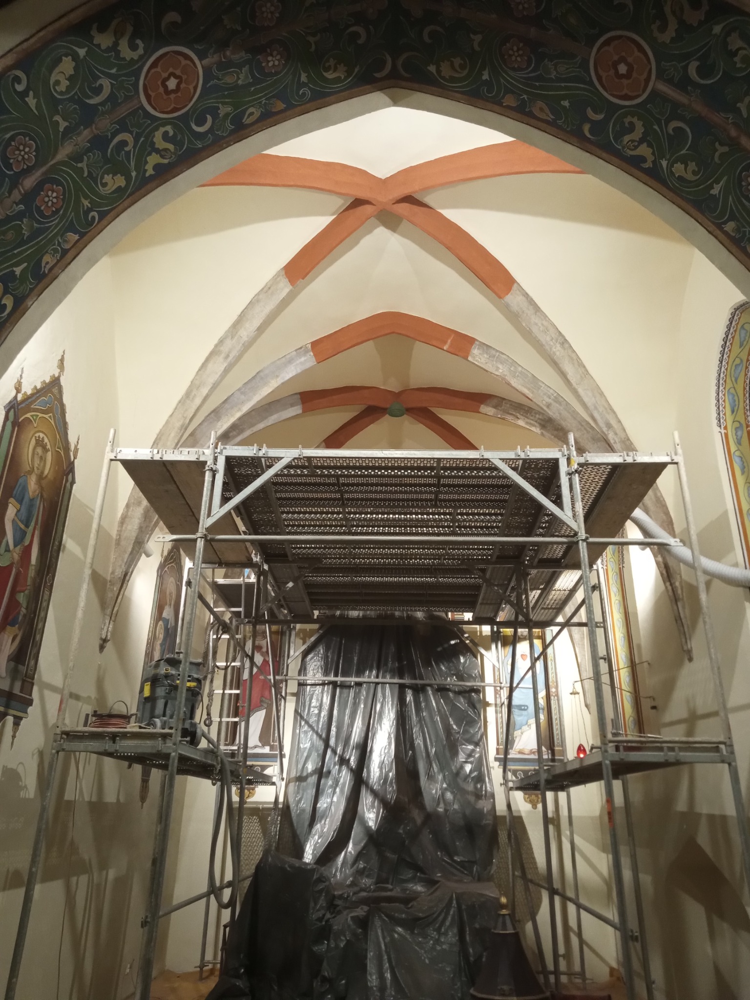 Wnętrze kościoła z rusztowaniem podczas prac konserwatorskich, zabezpieczona folią rzeźba, widoczne malowidła na ścianach i suficie.